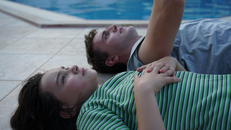 Image still from the movie Aftersun showing Calum and Sophie lying side by side next to a pool