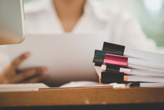Person working on unfinished paperwork with pen on busy office with pc computer.