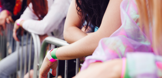 A group of people lined up against a barricade with multi colored wristbands on at an outdoor concert