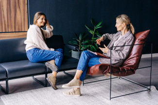 Two women sitting in a sofa and chair talking.