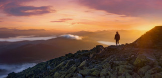 Person on top of mountain looking at sunset